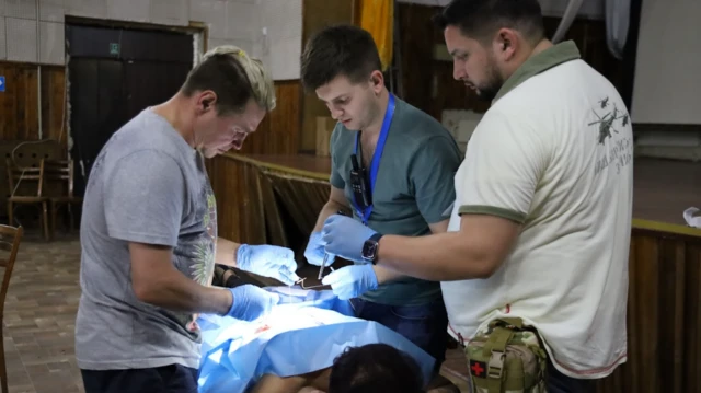 Una mujer tumbada boca abajo sobre una mesa con una sábana de operaciones azul sobre el cuerpo y tres médicos con guantes a su alrededor.