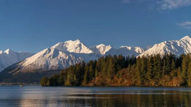 Cielo azul. Montañas blancas cubiertas de nieve. Un bosque y un lago.