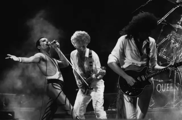 El grupo de rock británico Queen en concierto, de izquierda a derecha; Freddie Mercury (Frederick Bulsara, 1946 - 1991), John Deacon y Brian May.