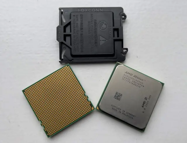 Las tres partes de un chip de AMD se ven puestas sobre un fondo blanco. Son tres piezas, una plástica de color negro, una verde con circuitos dorados, y uno verde con una pieza sólida de aluminio.
