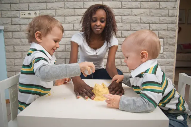 Mujer negra amasa sobre una mesa juntos a dos niños blancos