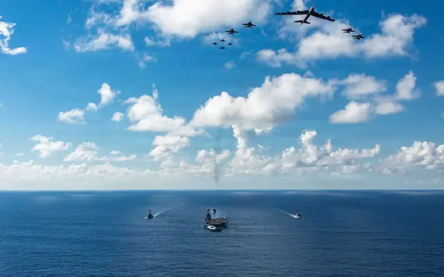 El USS Gerald Ford junto a sus escoltas en el Caribe, mientras que un grupo de aviones le pasan por encima.