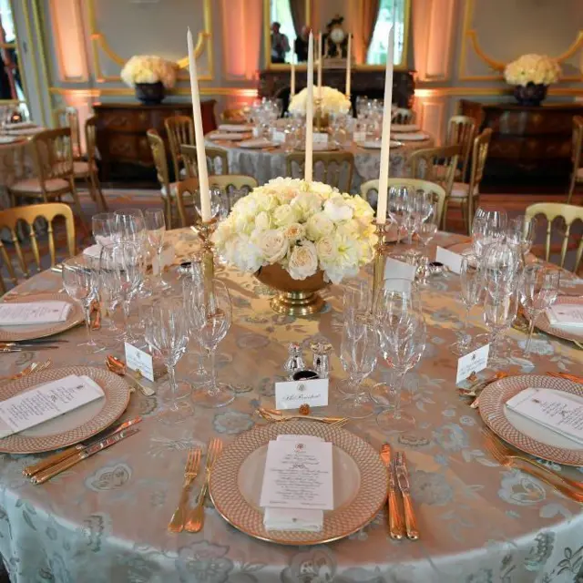 Una mesa de banquete redonda dispuesta para el servicio de cena con un arreglo floral redondo de rosas blancas en el centro de la mesa.