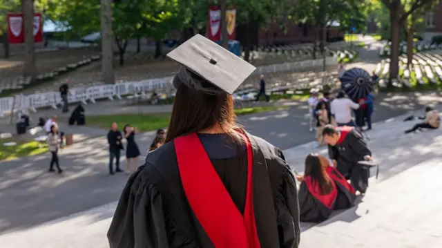 Una estudiante universitaria está de espaldas y viste una toga y birrete para una ceremonia de graduación