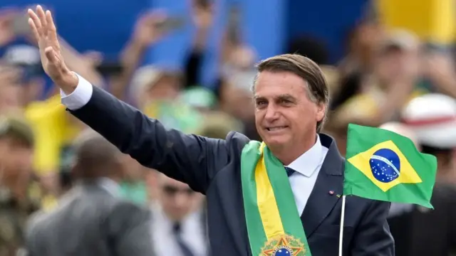 Jair Bolsonaro con la banda presidencial pardo junto a una bandera de Brasil