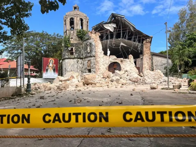 Una iglesia semiderruida detrás de una cinta amarilla que impide el paso.