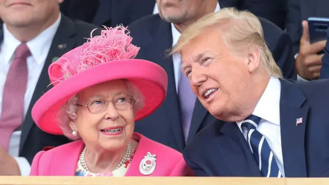 La reina Isabel, con sombrero y chaqueta rosas, sentada junto a un Trump que se inclina hacia ella en lo que parece ser una charla cordial. 