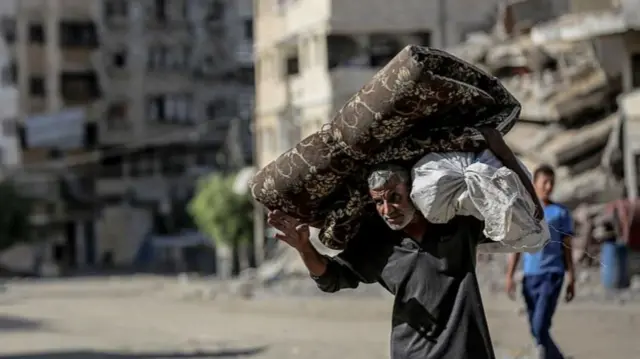 Un hombre carga grandes bultos a la espalda en una calle de Gaza