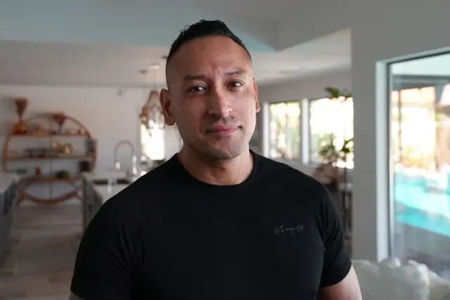 Tony Marquez está de pie en lo que parece ser la sala de una casa. Lleva puesta una camiseta negra.