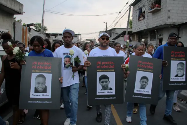 Personas que llevan carteles con las fotos de los cuatro de Guayaquil.