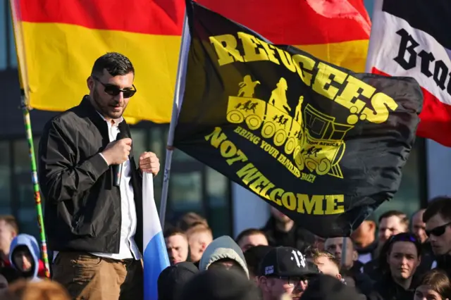 Simpatizantes en un acto de AfD junto a una bandera que afirma en inglés