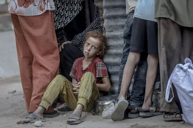 Una niña palestina espera sentada al lado de una olla vacía a recibir alimentación