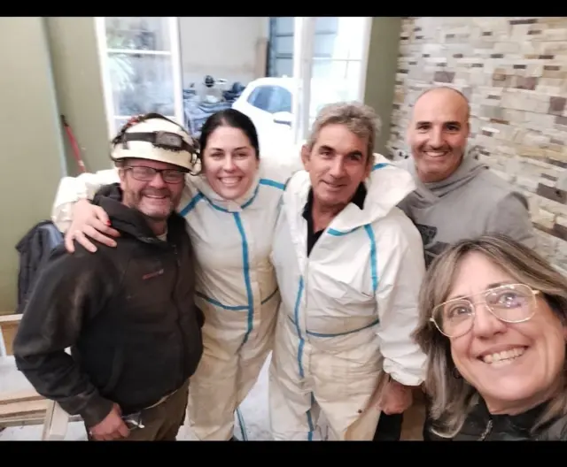 Vanessa Villegas, con un mono blanco, y otras personas posan sonrientes para un selfie en su casa devastada por las inundaciones.