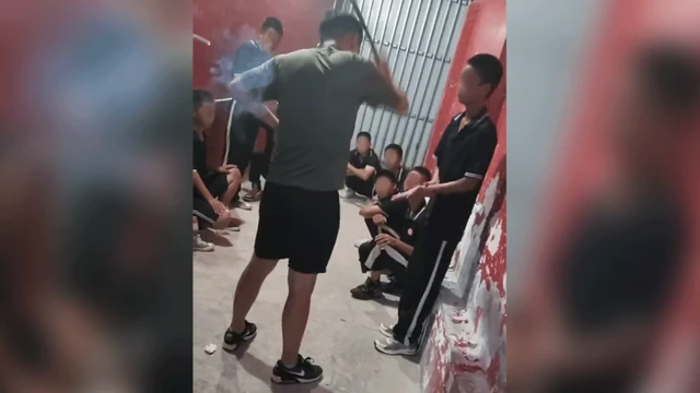 Una imagen fija de un teléfono móvil muestra la espalda de un instructor, de pie con una vara en alto, junto a un estudiante con la mano extendida