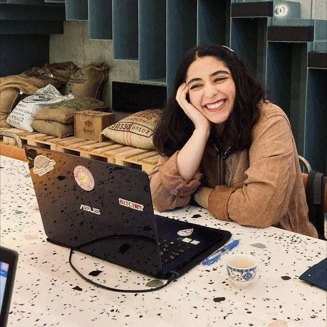 Parnia Abassi sonríe. Está sentada en una barra en una cafetería frente a su computadora