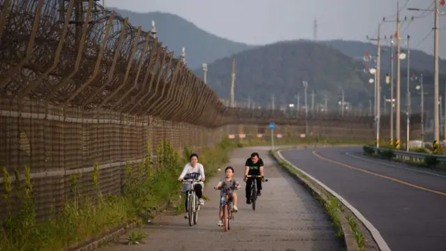 Personas en bicicleta a lo largo de una valla de alambre de púas de la Zona Desmilitarizada