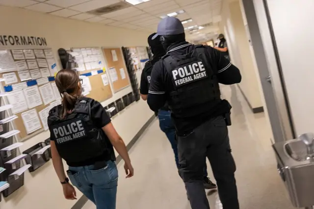 Tres agentes federales con chalecos balísticos caminan por un juzgado de Inmigración. 