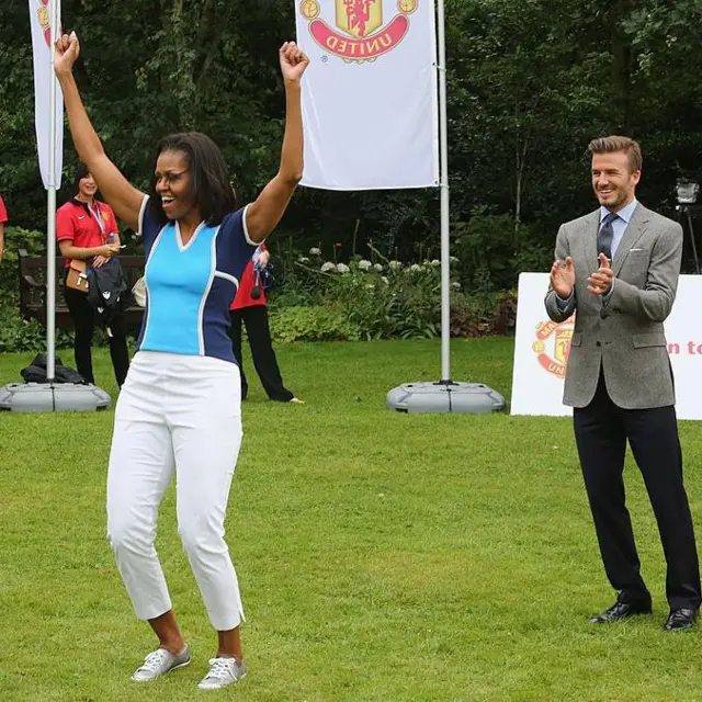 Michelle Obama levanta las manos y David Beckham está detrás de ella.