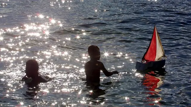 Niños jugando en el mar con un barco de juguete