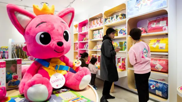 Los clientes ojean juguetes mientras se exhibe una muñeca gigante del personaje del zorro Pinkfong de la compañía en la tienda de la empresa en Corea del Sur.