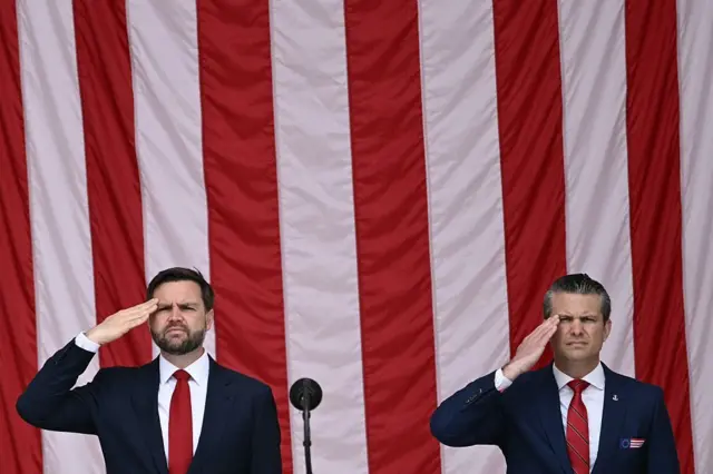 Pete Hegseth (der.) y JD Vance (izq.) en un saludo militar con la bandera de EE.UU. en el fondo
