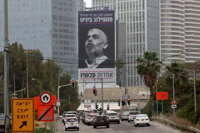 Los coches en Tel Aviv pasan junto a un cartel de Sinwar, con un mensaje en hebreo que insta a los israelíes a unirse contra su enemigo más buscado