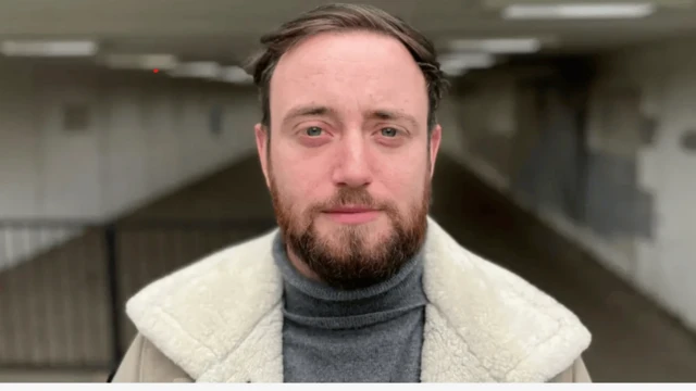 Retrato de Jacob Dunne, vistiendo una chaqueta y debajo de ella un sweater gris.