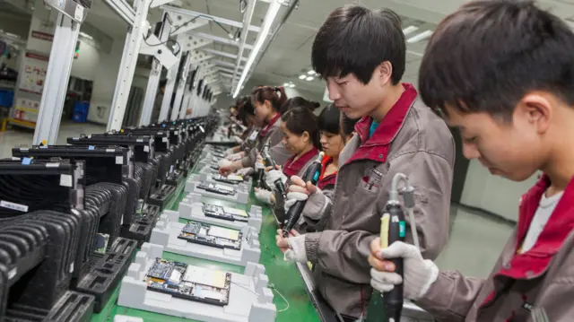 Una línea de hombres y mujeres ensambla dispositivos electrónicos