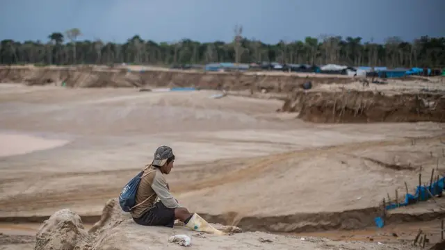 Un hombre sentado en el suelo junto a una mina clandestina en la Amazonía peruana.