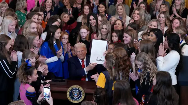 El presidente de EE.UU., Donald Trump, acompañado de atletas mujeres, muestra la orden ejecutiva recién firmada y titulada