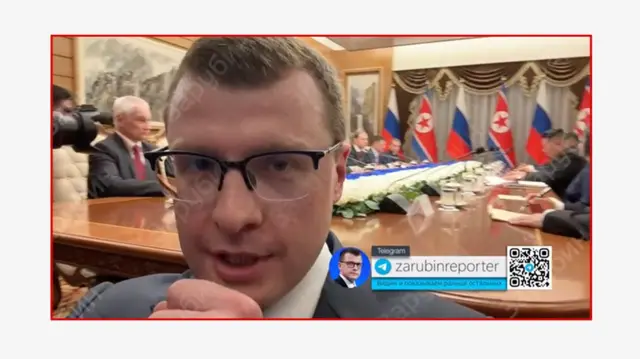 Zarubin informa desde una reunión de delegaciones de Rusia y Corea del Norte. Se ve su cabeza de frente. Al fondo, los dignatarios de Rusia y Corea del Norte están sentados en la mesa de reuniones.