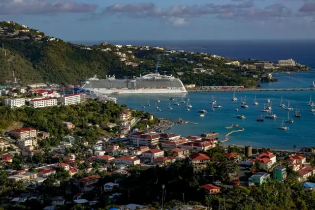 Panorámica actual del puerto de Saint Thomas, con pequeñas embarcaciones y un gran crucero sobre un mar azul y un cielo igual de azul. 