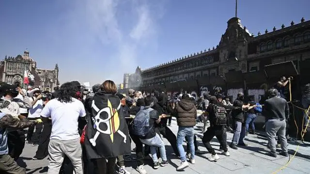 Personas intentan derribar las vallas que protegen el Palacio Nacional en la Plaza del Zócalo.