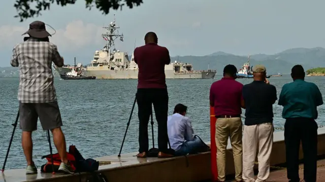 El 30 de octubre de 2025, la gente observaba y fotografiaba al USS Gravely, un buque de guerra de la Armada estadounidense, zarpando del puerto de Puerto España.