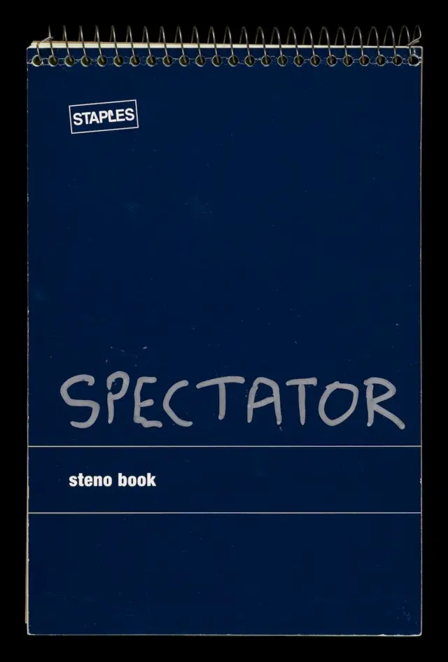 Un cuaderno de espiral azul, con la palabra Spectator escrita en el frente con bolígrafo plateado.