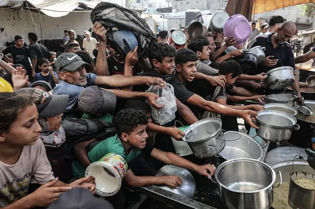 Un grupo de palestinos extiende las ollas que sujetan con la esperanza de recibir comida en un campo de refugiados en el centro de Gaza. 