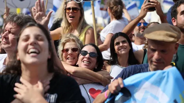 Israelíes sonrientes celebran la liberación de los rehenes, que siguen en pantallas gigantes instaladas en la Plaza de los Rehenes de Tel Aviv.