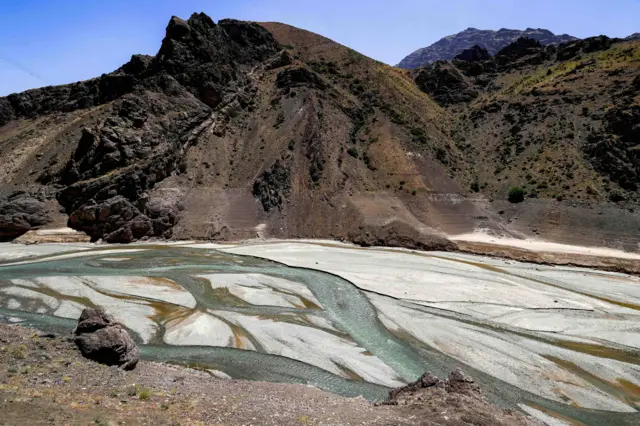 La entrada de agua baja del río aguas arriba de la presa Amir Kabir a lo largo del río Karaj se muestra en la cordillera de Alborz, en el norte de Irán, el 1 de junio de 2025: hay canales de agua que se abren paso a través de depósitos que ocupan un área más amplia que el agua.