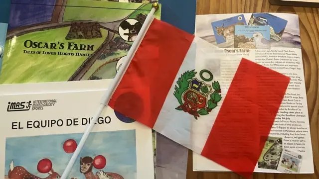 Una bandera peruana -con dos franjas rojas y una blanca y un escudo verde en el centro- sobre unos libros infantiles 
