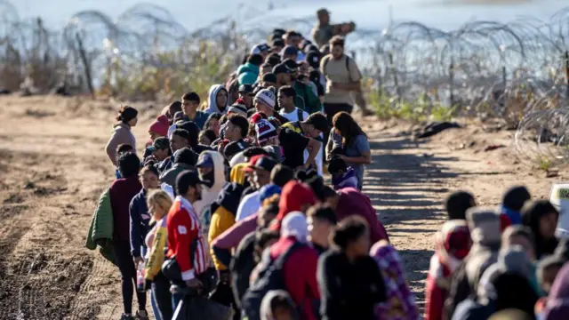 Un grupo de migrantes espera en fila cerca de un centro de procesamiento de campo de la Patrulla Fronteriza de Estados Unidos después de cruzar el Río Grande desde México el 18 de diciembre de 2023 en Texas.