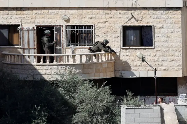 Un soldado desde un balcón apunta a un hombre que se encuentra en el piso inferior