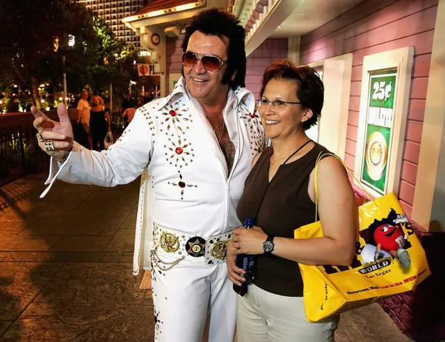 El imitador de Elvis Presley Tom E. Lynd (izquierda) posa para una foto con la turista canadiense Brenda Rediron en el Strip el 28 de junio de 2005 en Las Vegas, Nevada. Lynd es dueño de Legends in Photos, un grupo de imitadores que se presentan en el Strip y posan con los turistas a cambio de propinas. (Foto de Ethan Miller/Getty Images)