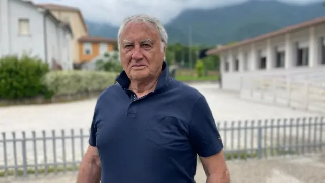 El alcalde Giacomo de Luca, un hombre con una camisa de manga corta azul oscura, parado frente a unos edificios  