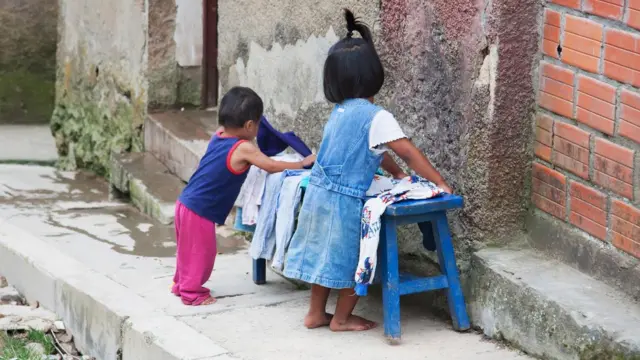 Una niña y un niño juegan en la puerta de una casa. 