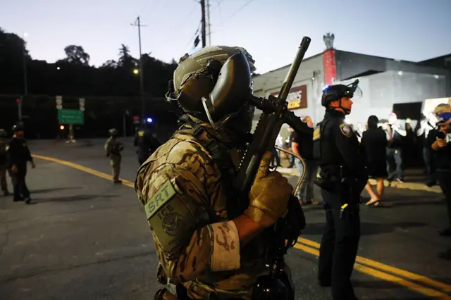 Un agente del Servicio de Inmigración y Control de Aduanas (ICE), uniformado, con un arma de gran porte en su mano derecha.