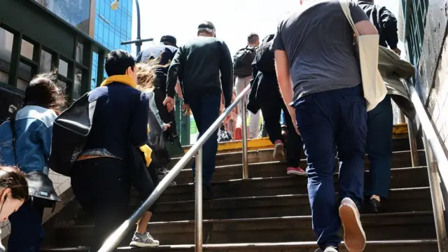 Varias personas subiendo las escaleras de un subterráneo en la ciudad.