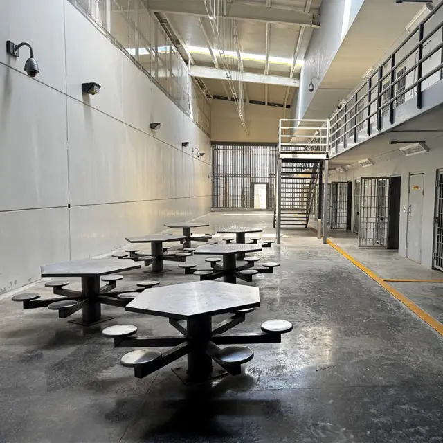 Interior de la sección de máxima seguridad con mesas, sillas de acero y celdas pequeñas.