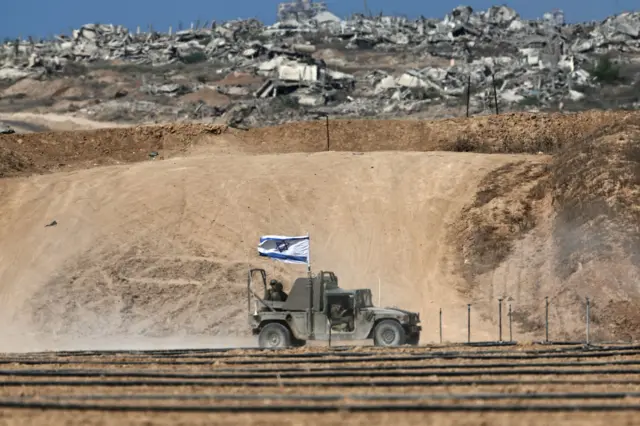 Un vehículo militar israelí con una bandera del país pasa por delante de unas ruinas en Gaza.