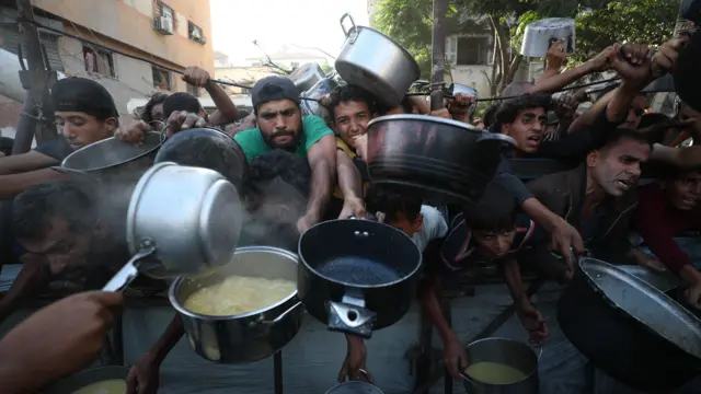 Gazatíes sosteniendo cacerolas para intentar acceder a alimentos.