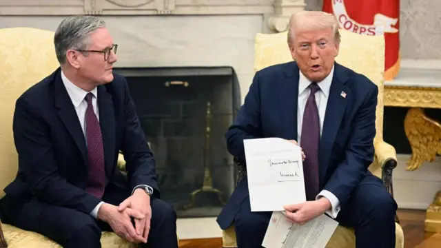 El presidente Trump muestra una carta del rey Carlos III durante su reunión en el Despacho Oval con el primer ministro británico, Keir Starmer. Trump y Starmer están sentados el uno junto al otro y ambos visten traje oscuro y corbata. 